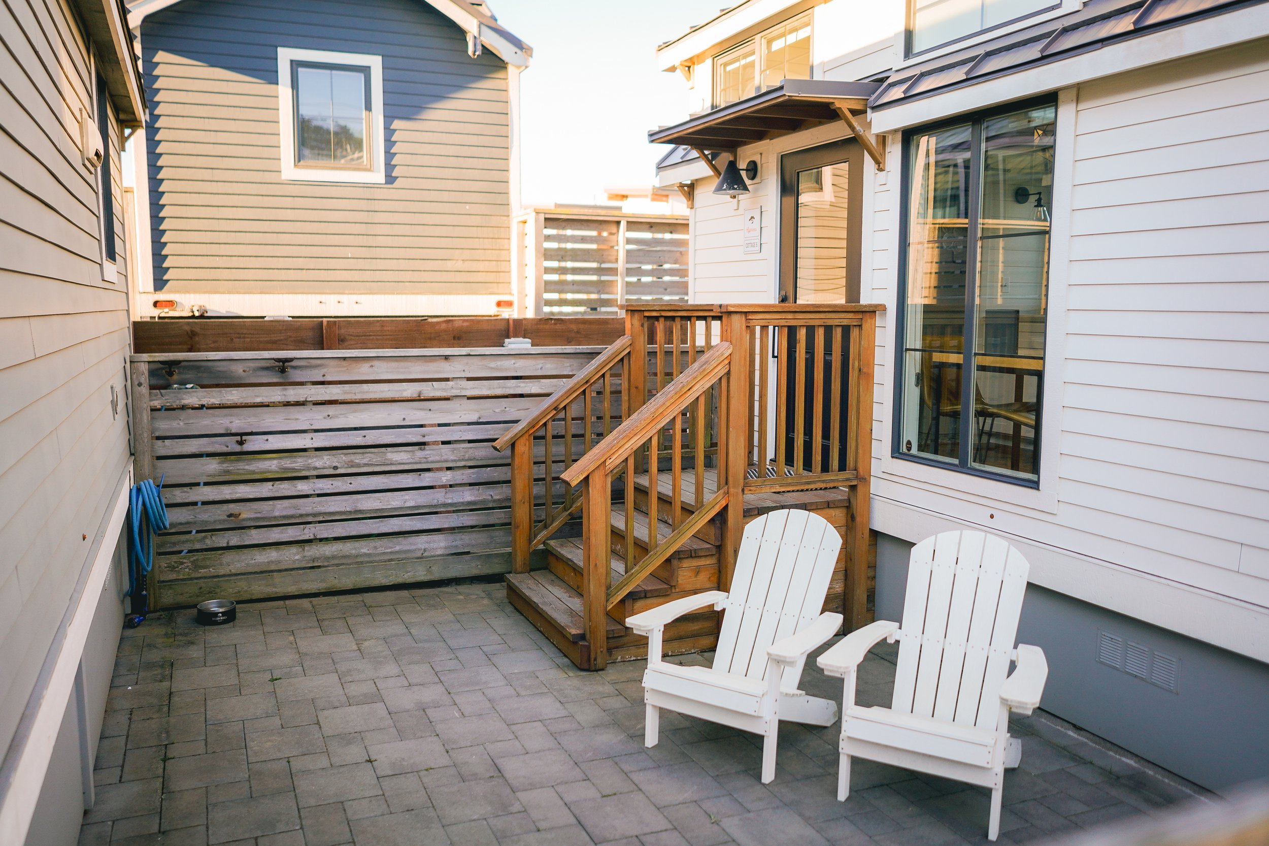 Private paved patio area of a Cypress Cottage featuring two white Adirondack chairs and wooden fencing.