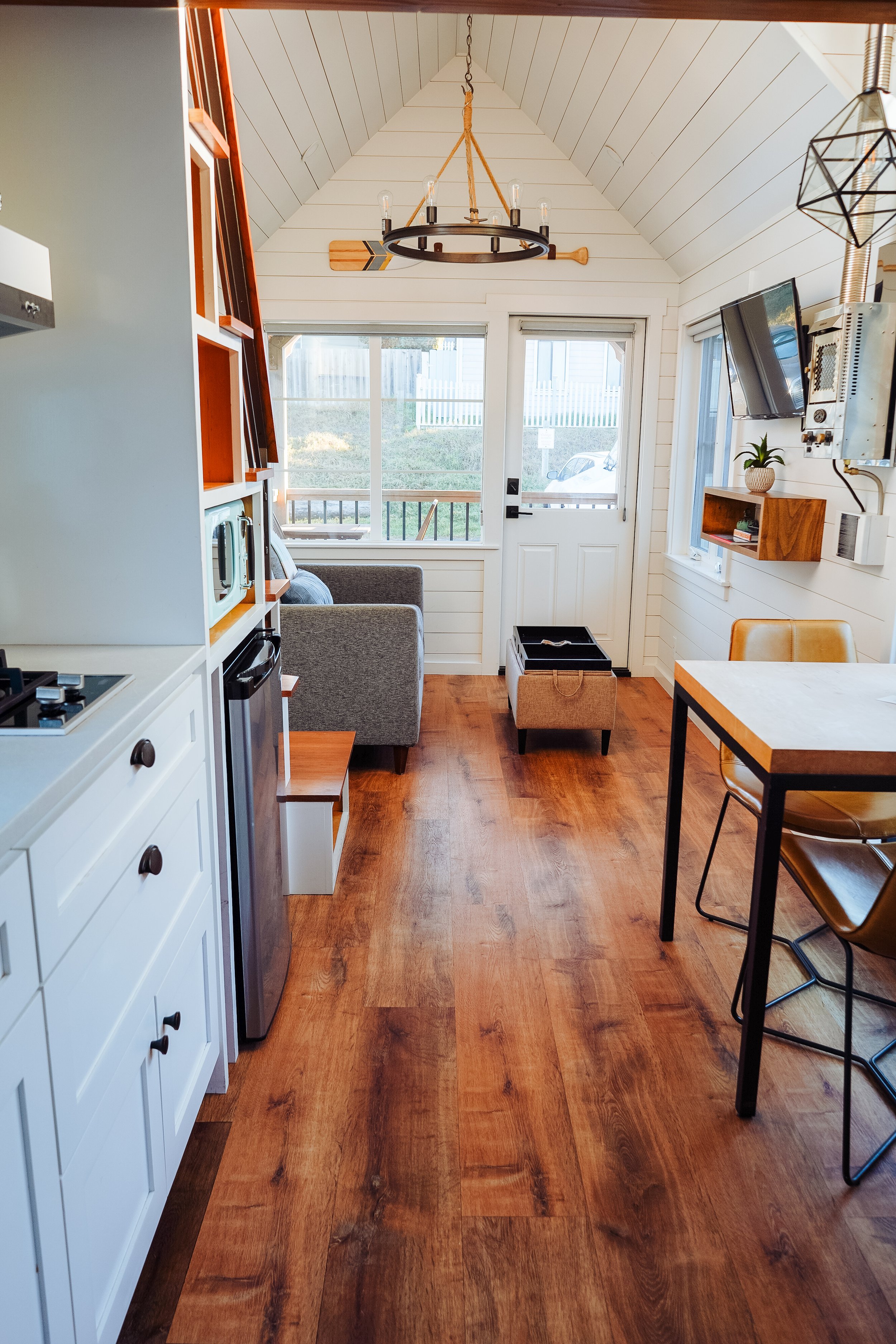 Bright living area of a tiny home with a sliding barn door, wooden stairs, and a leather sofa.