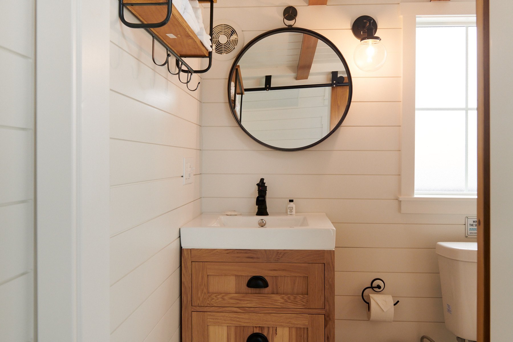 Bright bathroom at ブライトリビエラ featuring a white and blue vintage-style wall-mount sink, white shiplap walls, and a wooden towel rack with wicker storage baskets.