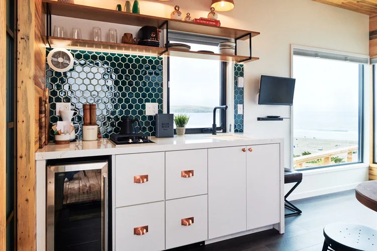 Modern open-concept kitchen in an Osprey cabin with a light wood dining table, leather chairs, copper pendant lights, and a white Smeg-style refrigerator.