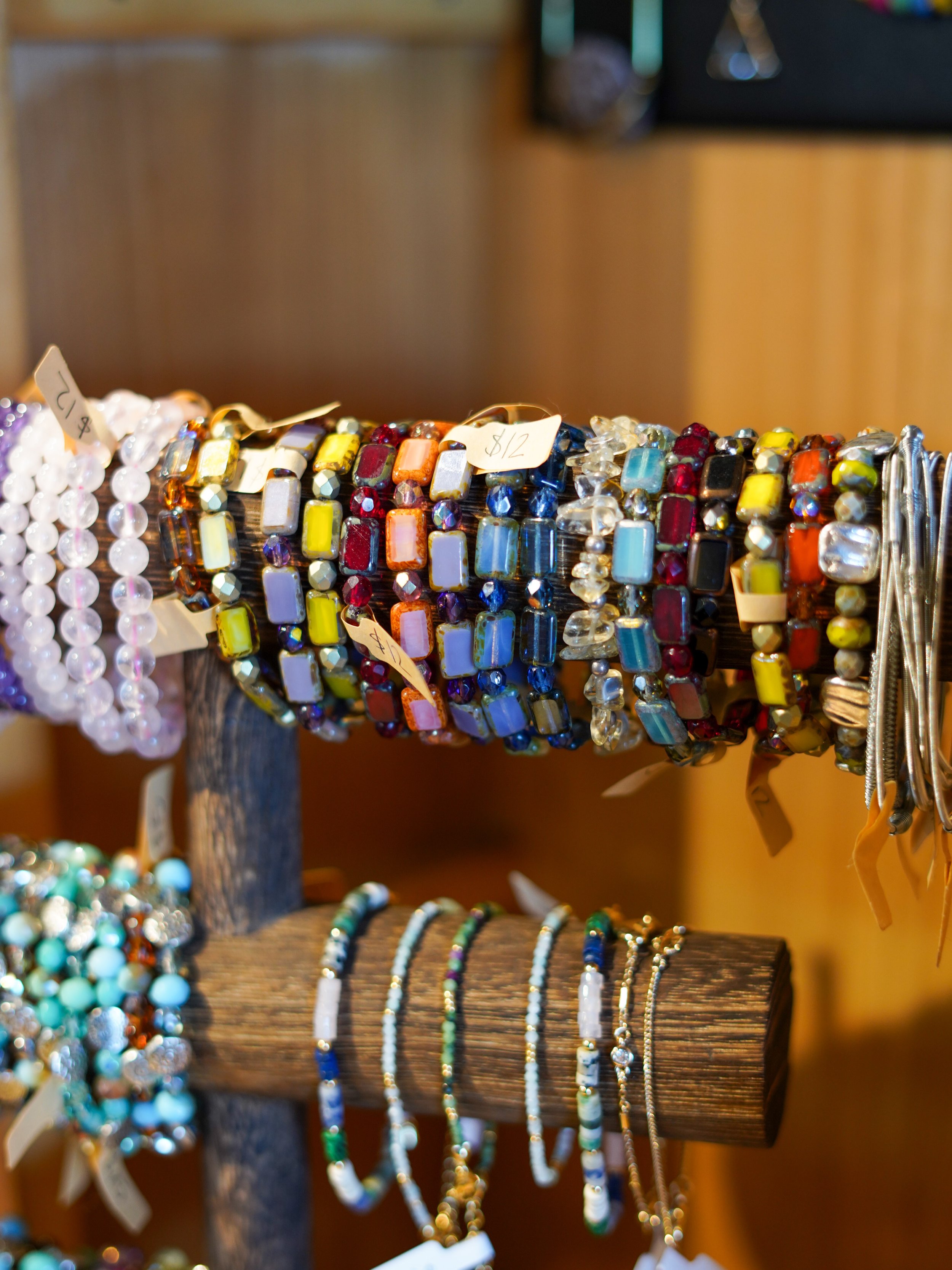 Colorful beaded bracelets and necklaces displayed on wooden stands at a craft fair.
