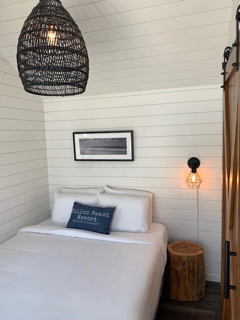 A cozy sleeping loft in a Sweetwater cabin with a whale-patterned comforter, low vaulted ceilings, and white wood paneling.