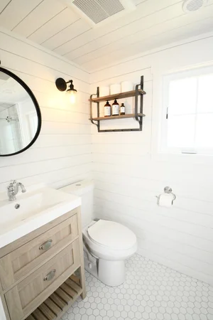 Modern bathroom interior of a Sweetwater cabin with white shiplap walls, a circular black-framed mirror, and a wood-tone vanity with a white vessel sink.