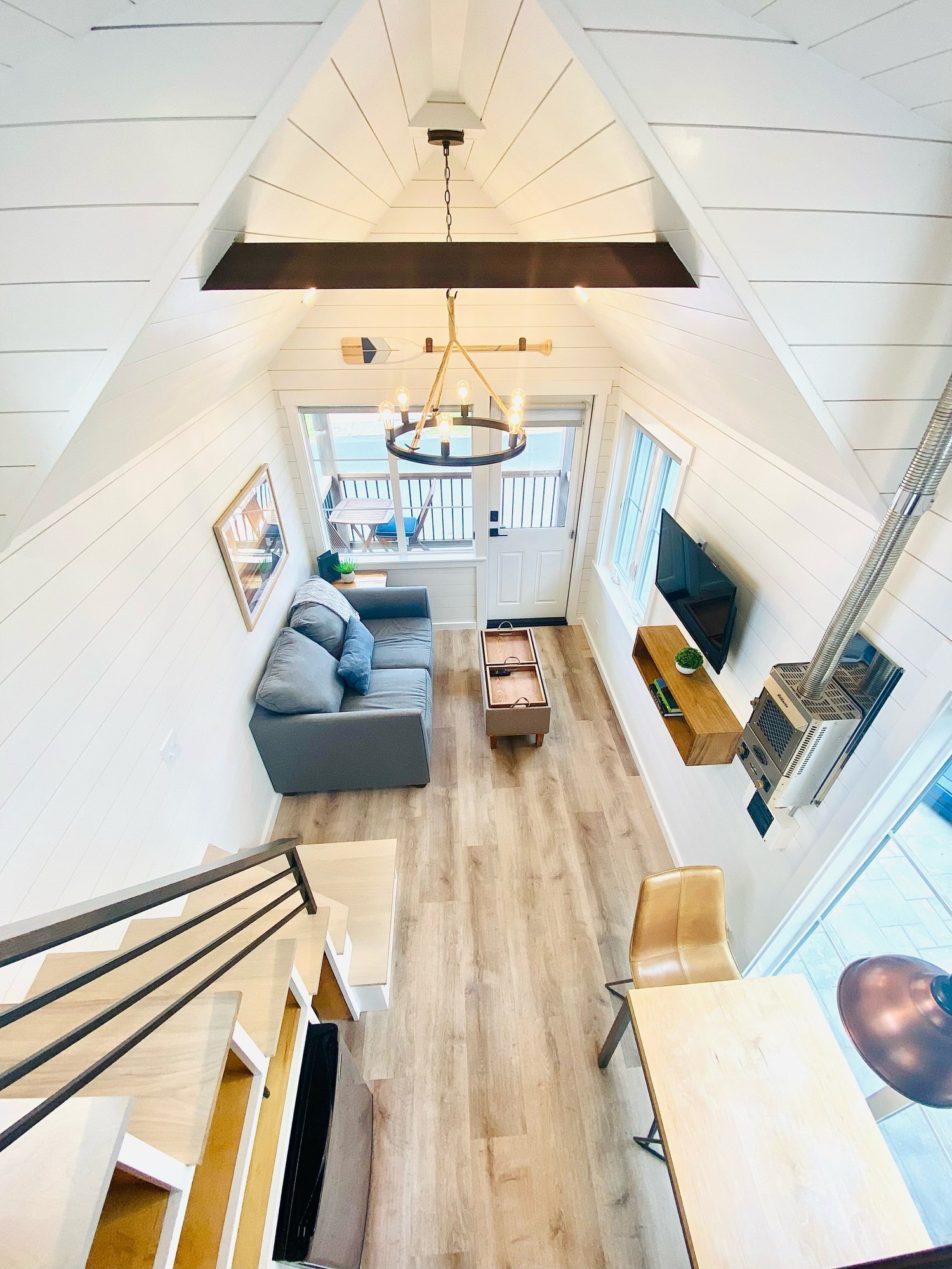 High-angle view of a tiny house living room featuring vaulted ceilings, a grey sofa, and hardwood flooring.
